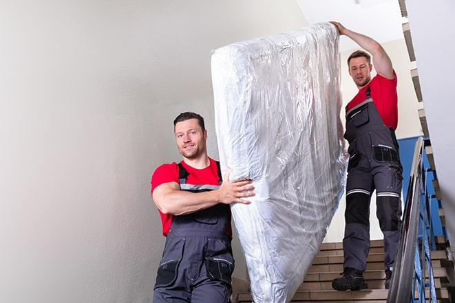 two workers carrying a heavy box spring out of a bedroom in Frontenac